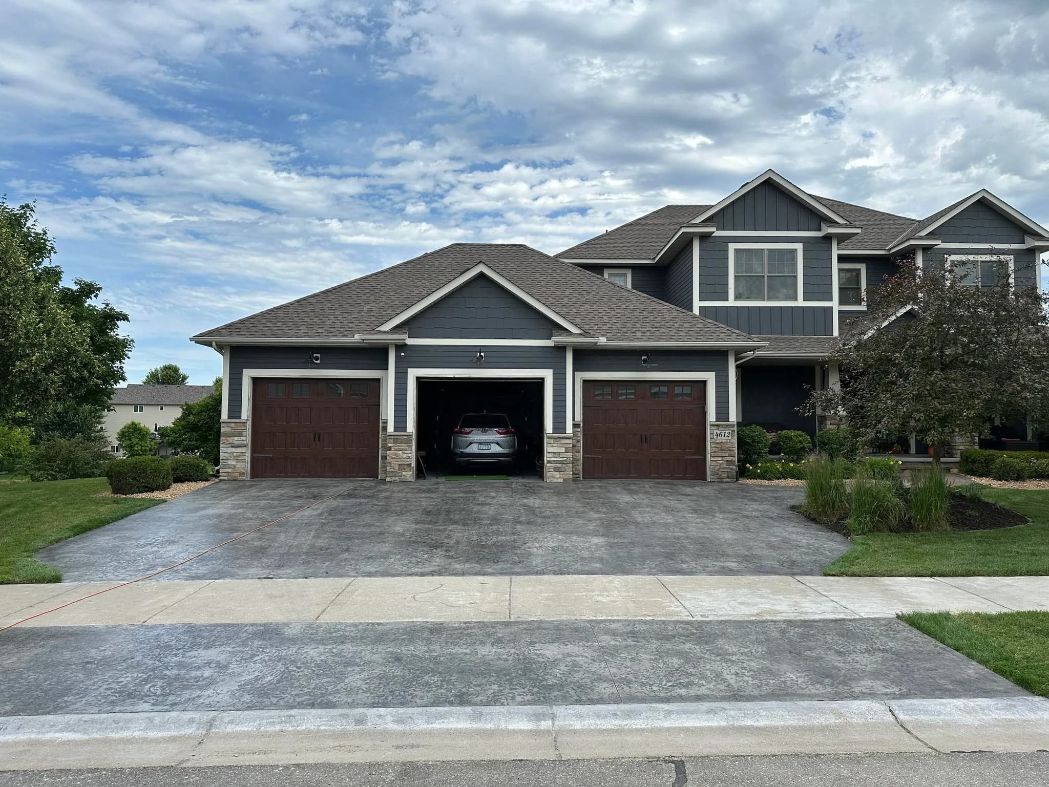 Three-car concrete driveway leading to a craftsman-style blue home, installed by Mason's Stamping & Concrete in the Albertville, Minnesota area